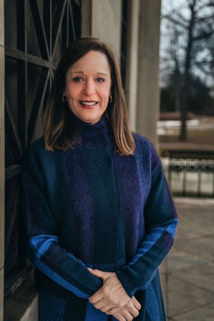 A woman in a blue coat is standing in front of a building.