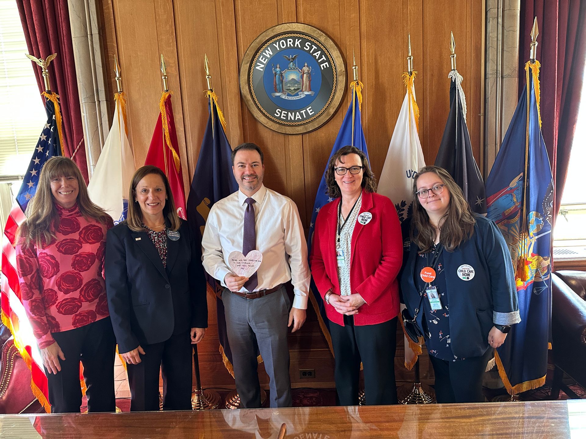 A group of people are standing around a table in front of flags.