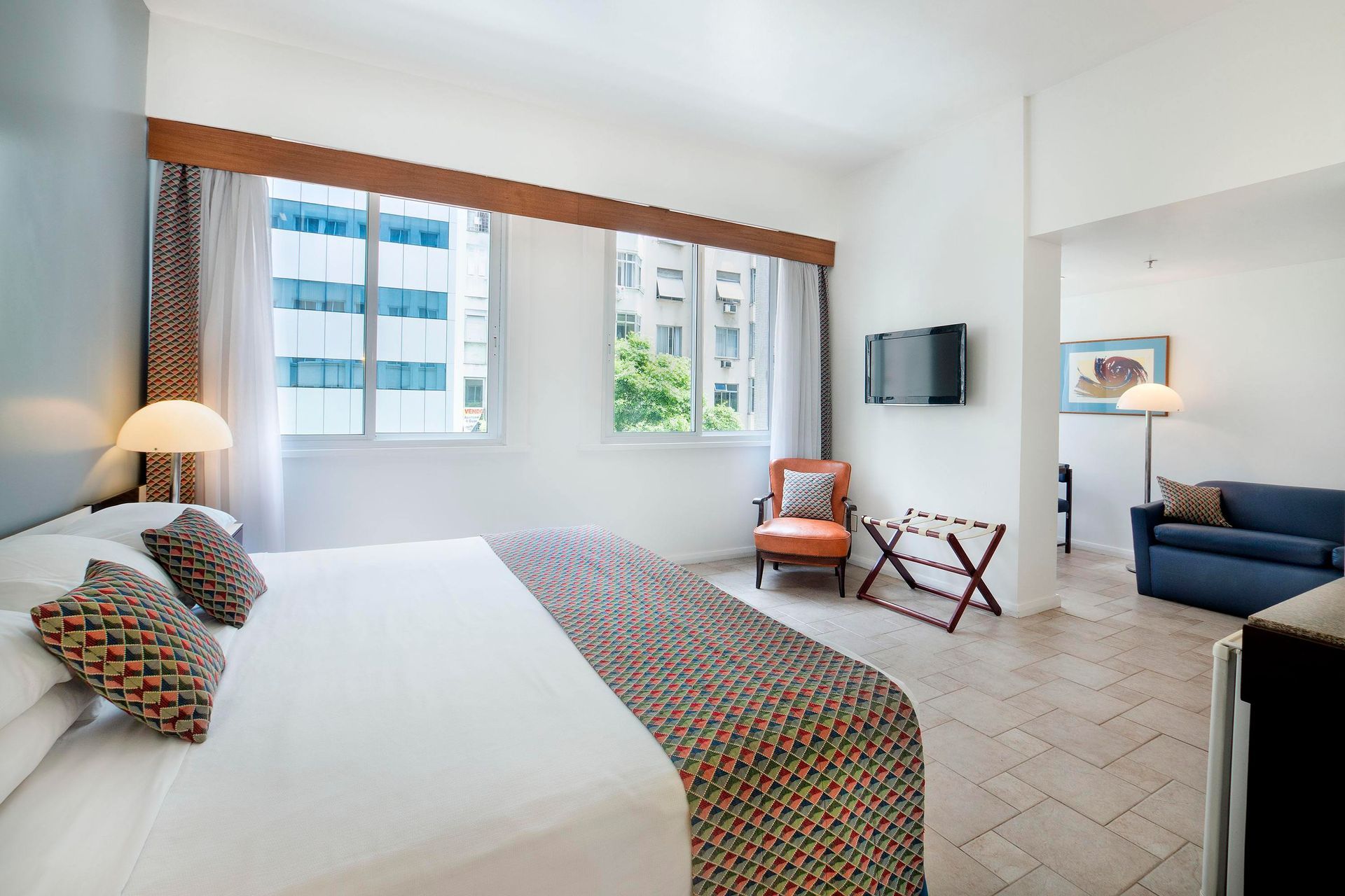 Um quarto de hotel com uma cama king size, sofá, cadeira e televisão.
