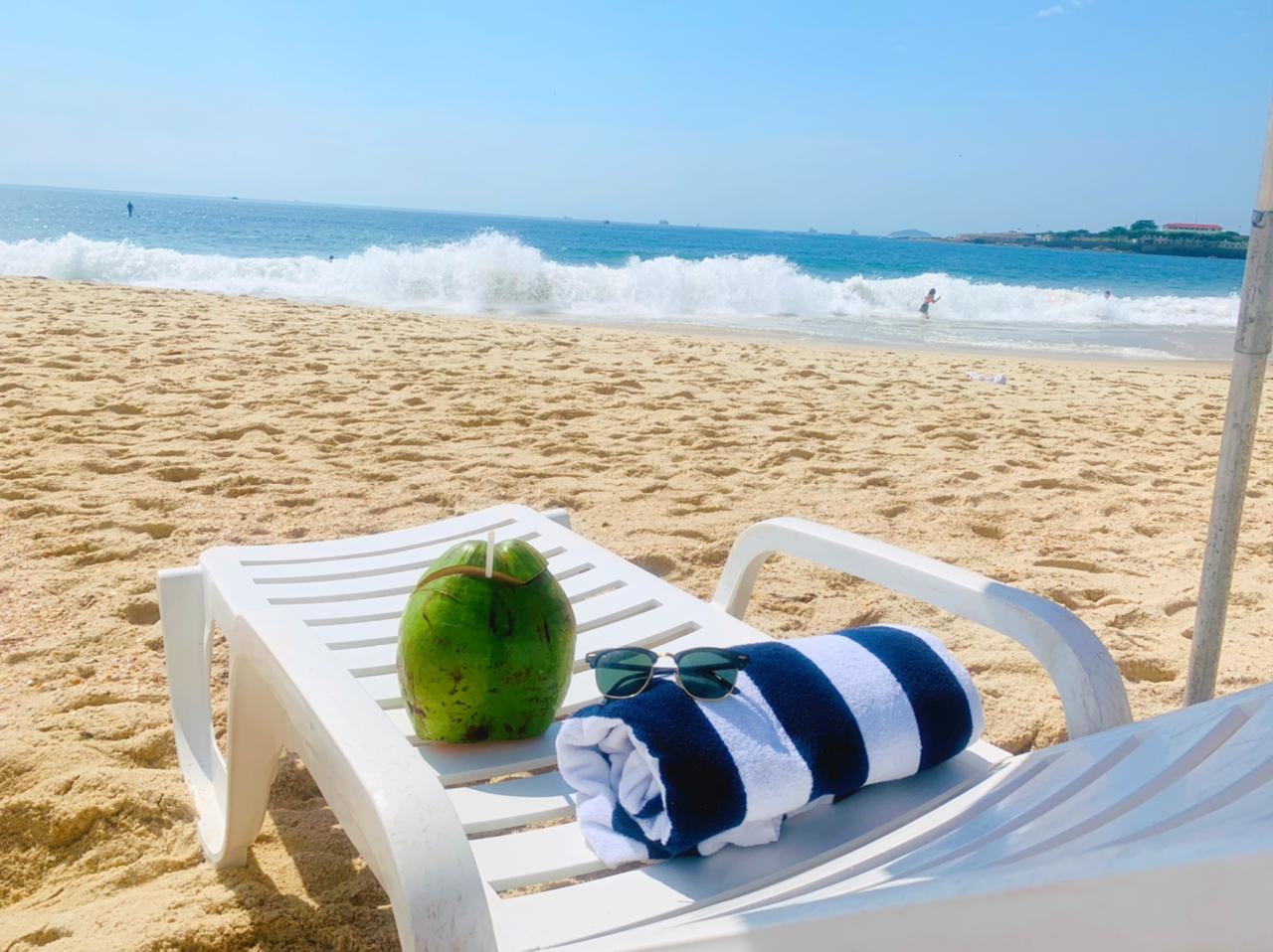 Uma cadeira de praia com uma toalha, óculos escuros e um coco.