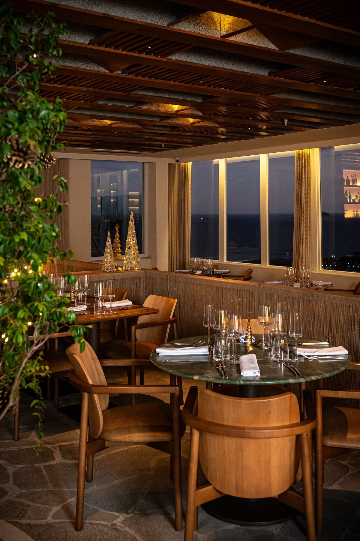 Uma tigela de flores está sobre uma mesa em frente a uma janela com vista para o oceano.