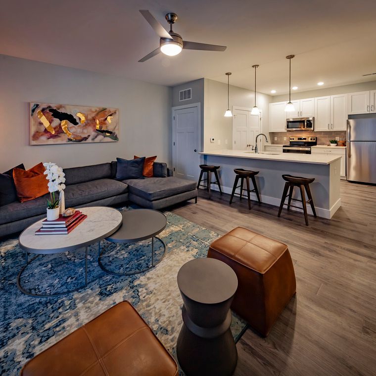 A living room with a couch , coffee table , stools and a ceiling fan.