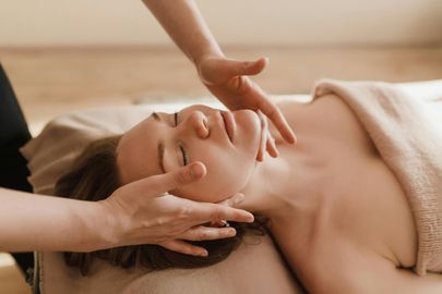 A woman is laying on a bed getting a massage on her face.