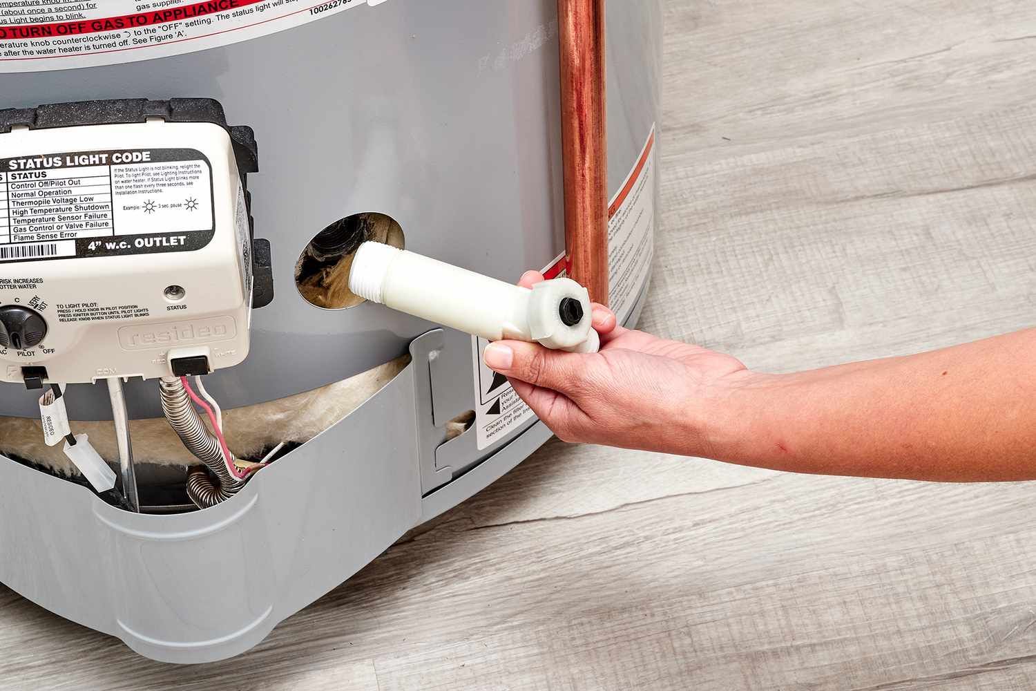 Plumber repairing a sink drain under a stainless steel kitchen sink, wearing gloves.
