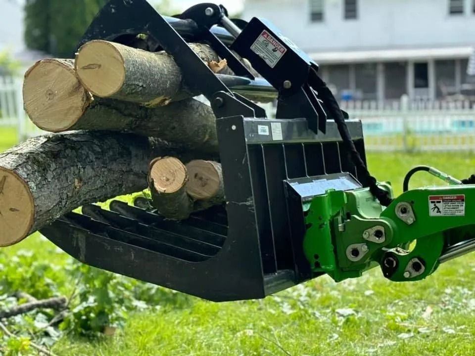 Black grapple on a green tractor holding several logs by Allen's Tree and Fence