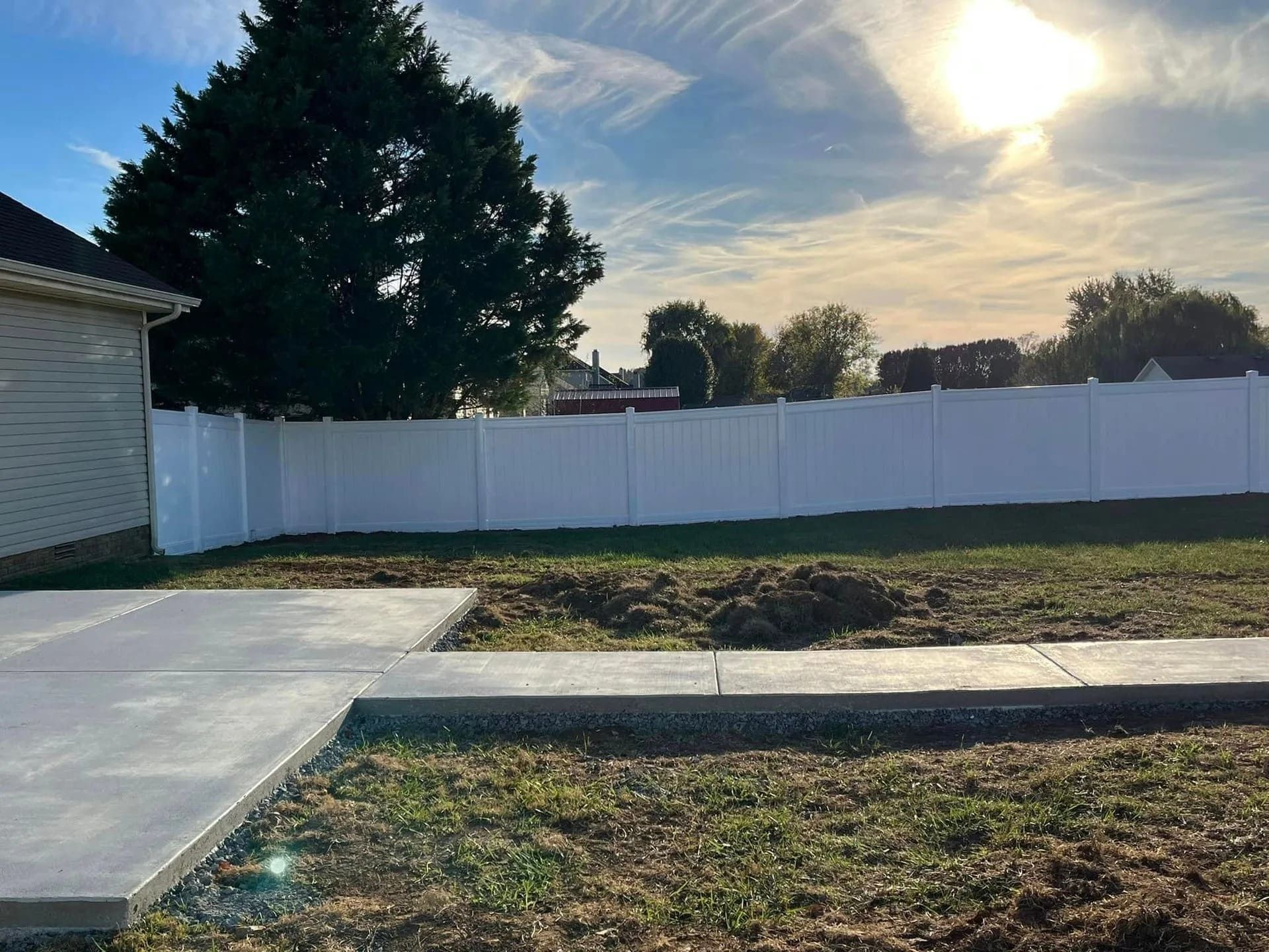 White vinyl fence surrounds a backyard with new concrete, by Allen's Tree and Fence.