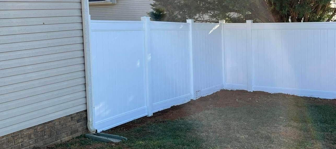 White vinyl fence in a backyard. The fence is near a house with gray siding and green grass.
