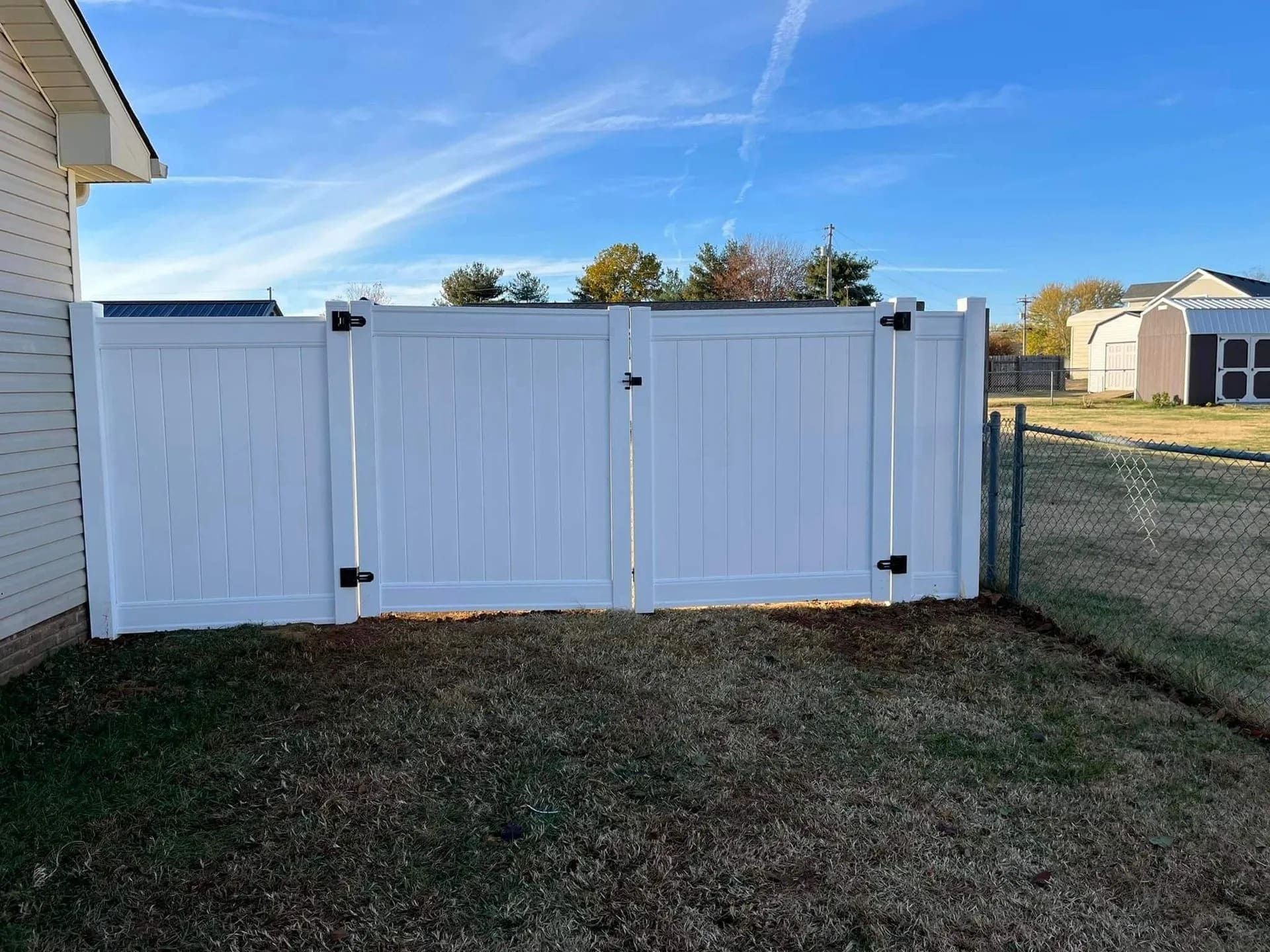 White vinyl fence with double gate in a grassy yard, under a blue sky by Allen's Tree and Fence