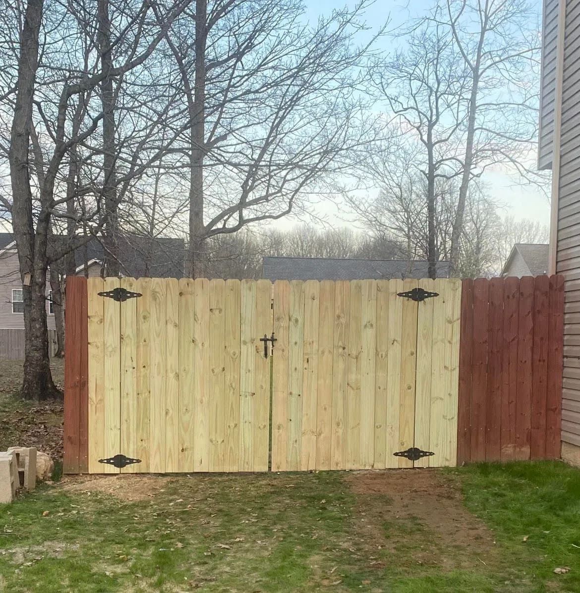 Wooden double gate in a backyard, with black hinges and latch by Allen's Tree and Fence.