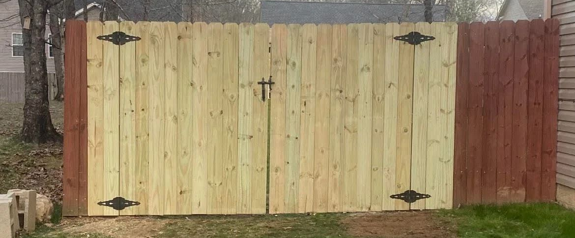 Wooden gate with black hardware and a red-stained fence section by Allen's Tree and Fence.