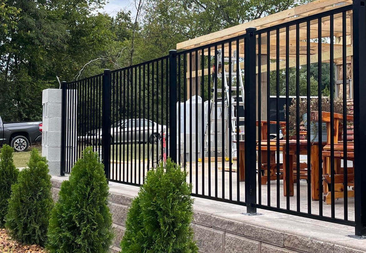Black metal fence with vertical bars, bordering a patio by Allen's Tree and Fence.