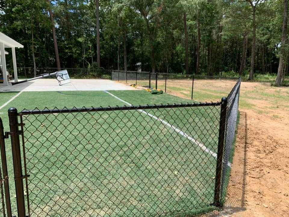 Black chain-link fence encloses a green turf area, and a patio by Allen's Tree and Fence.