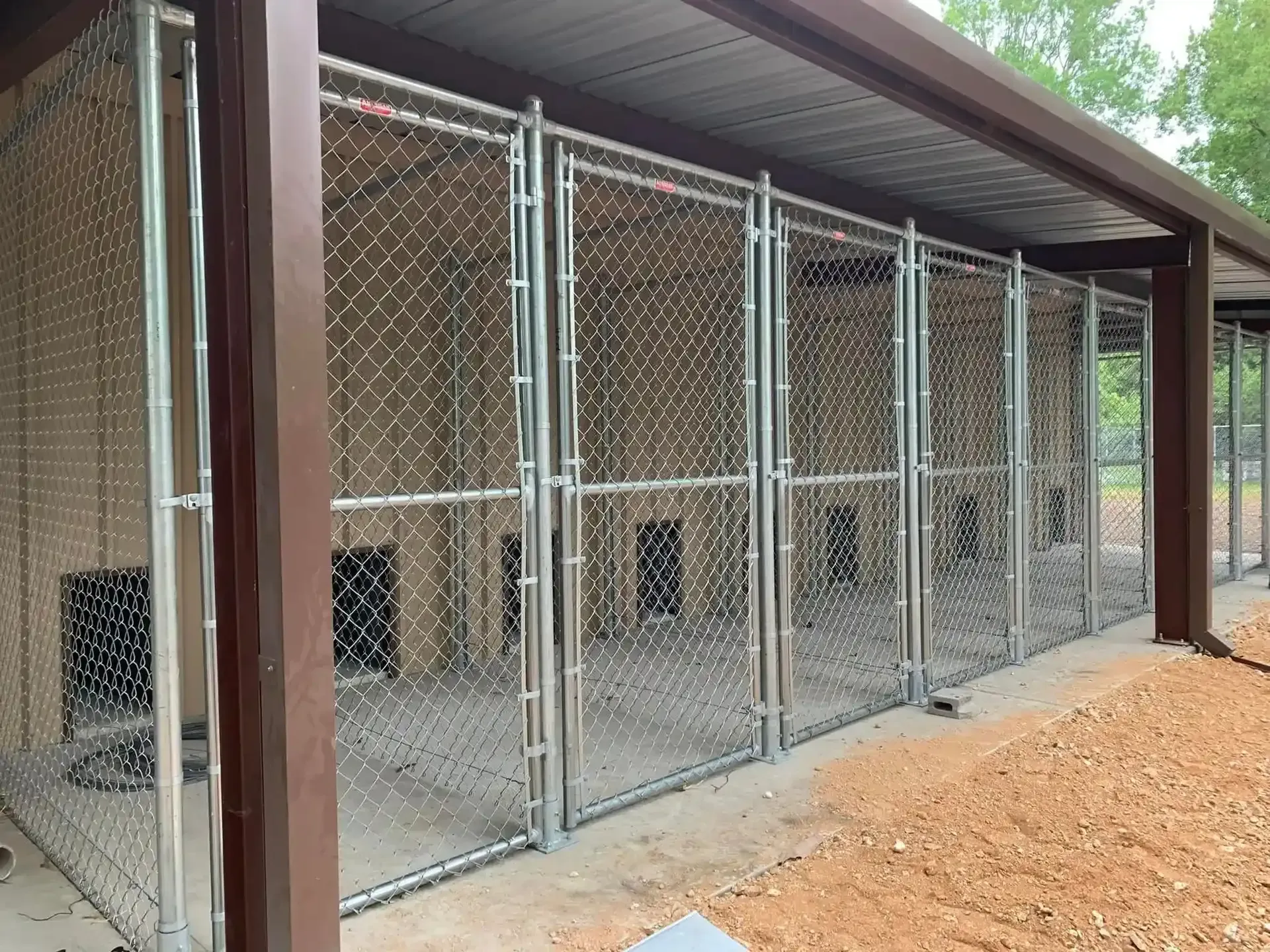 Chain link dog kennels under a brown-roofed structure, by Allen's Tree and Fence.
