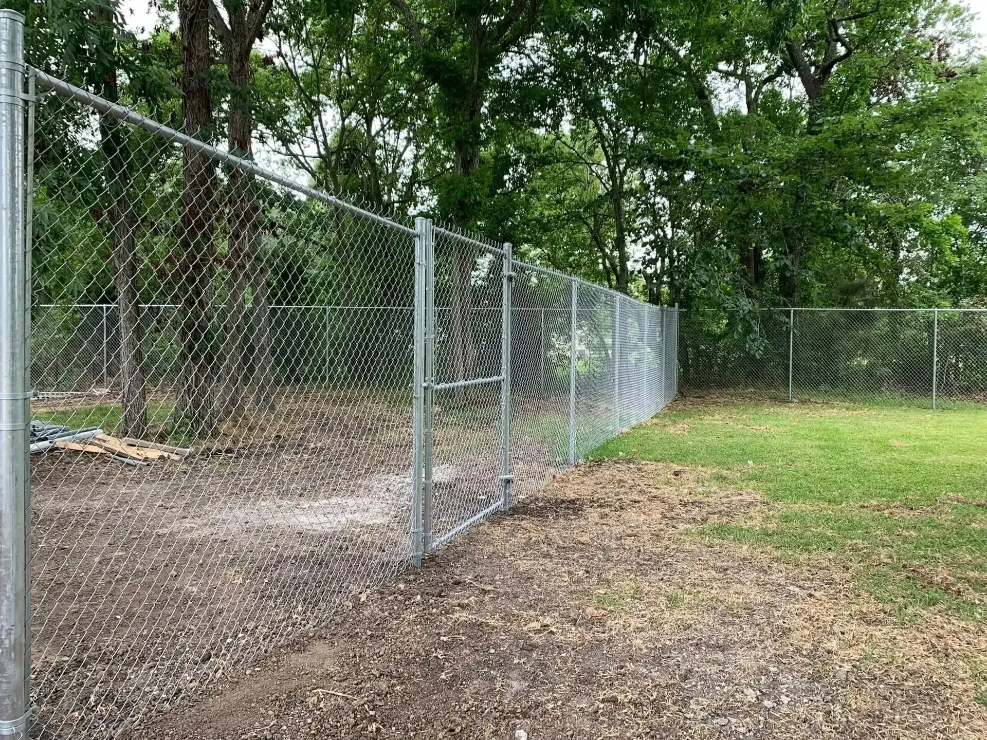 Chain-link fence with an open gate in front of a grassy yard by Allen's Tree and Fence.