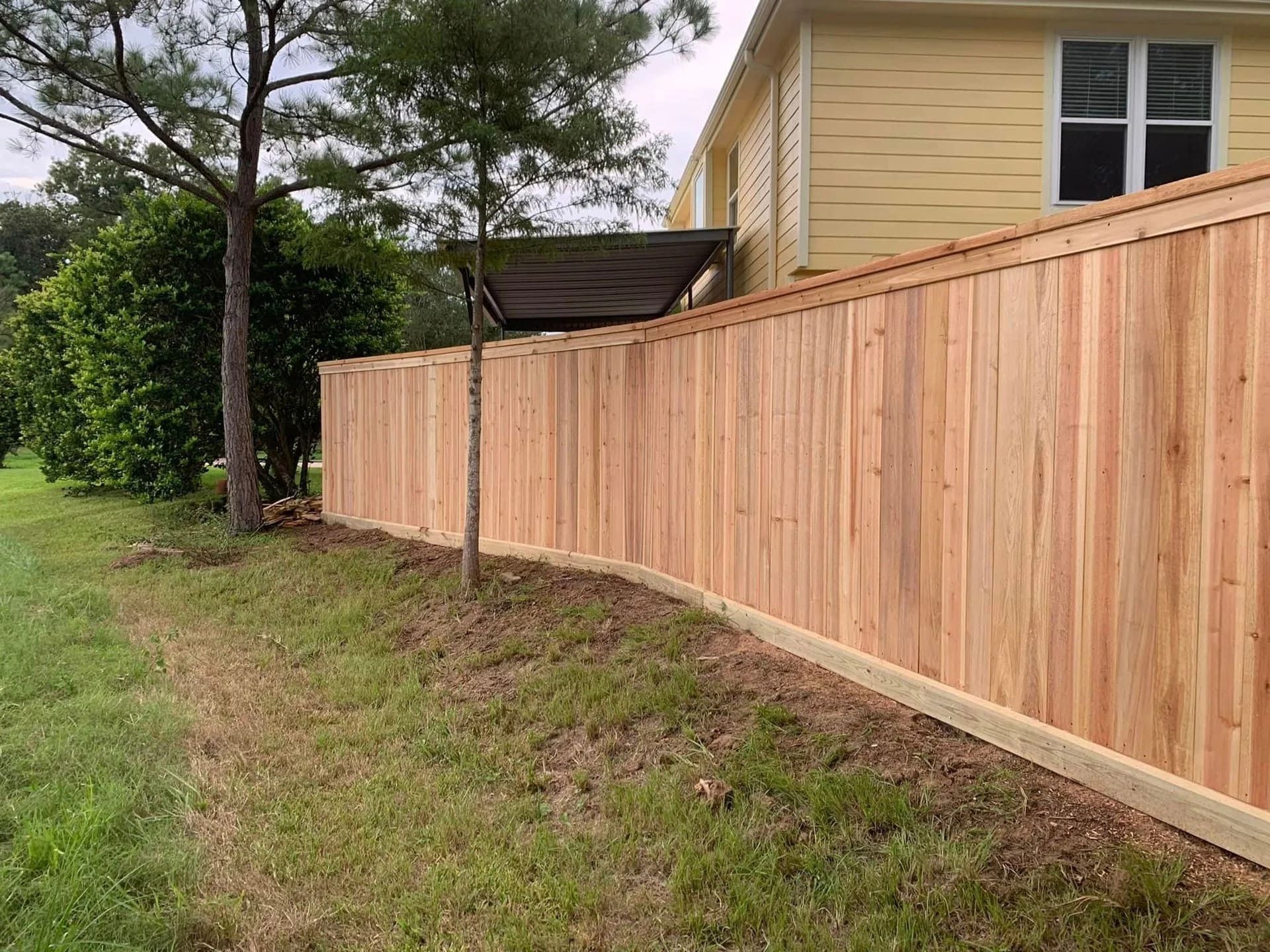 Wooden privacy fence along a grassy lawn next to a yellow house  by Allen's Tree and Fence.