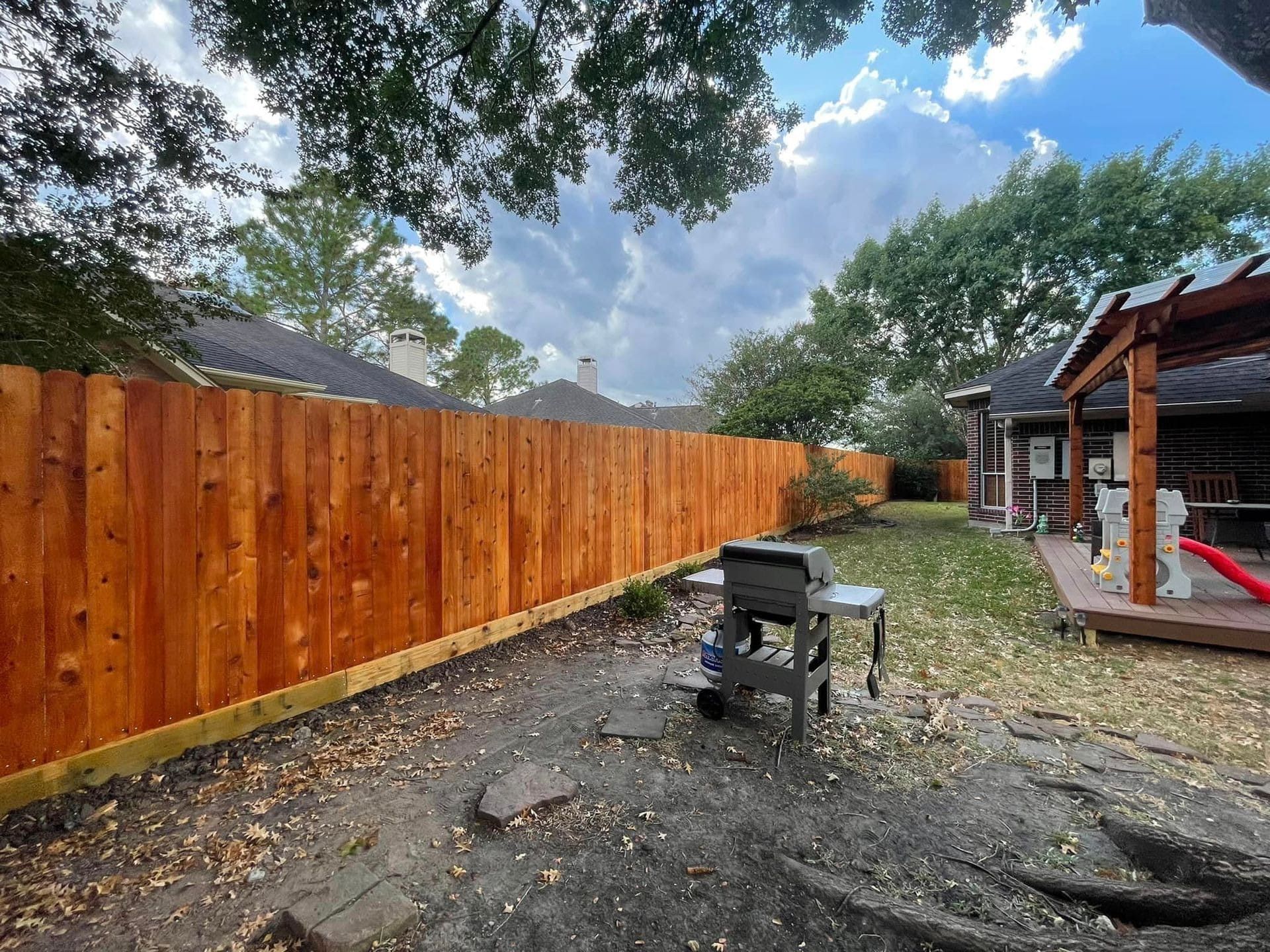 Wooden fence in a backyard with a grill, leaves, and a patio by Allen's Tree and Fence.