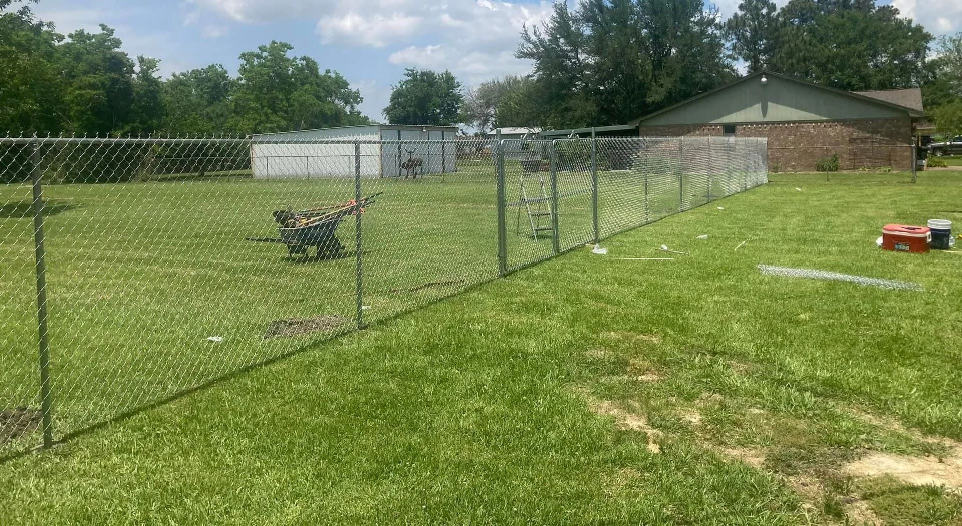 Chain-link fence in a grassy yard, with a house and trees, by Allen's Tree and Fence.