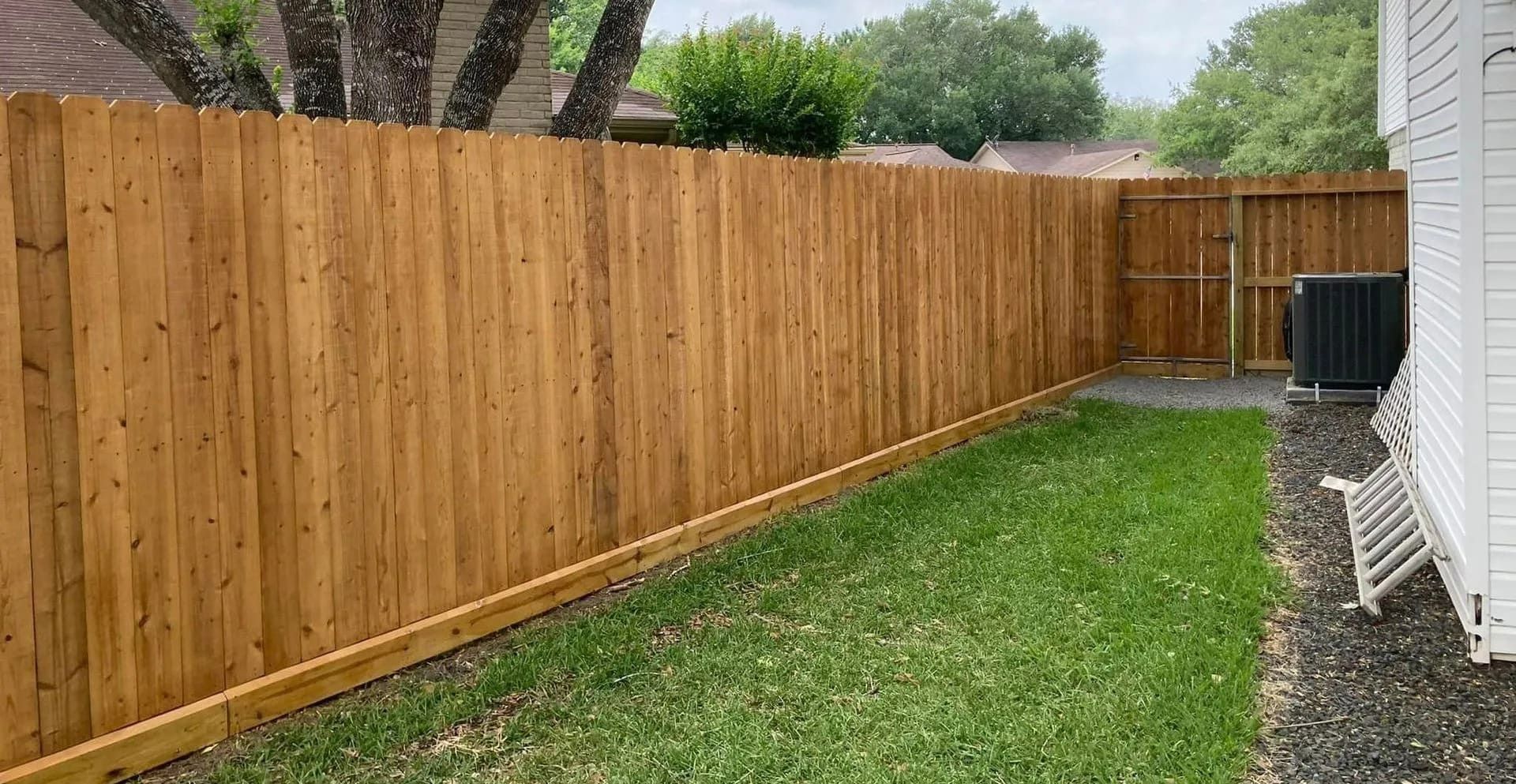 Wooden fence in backyard; green grass, air conditioner, by Allen's Tree and Fence.