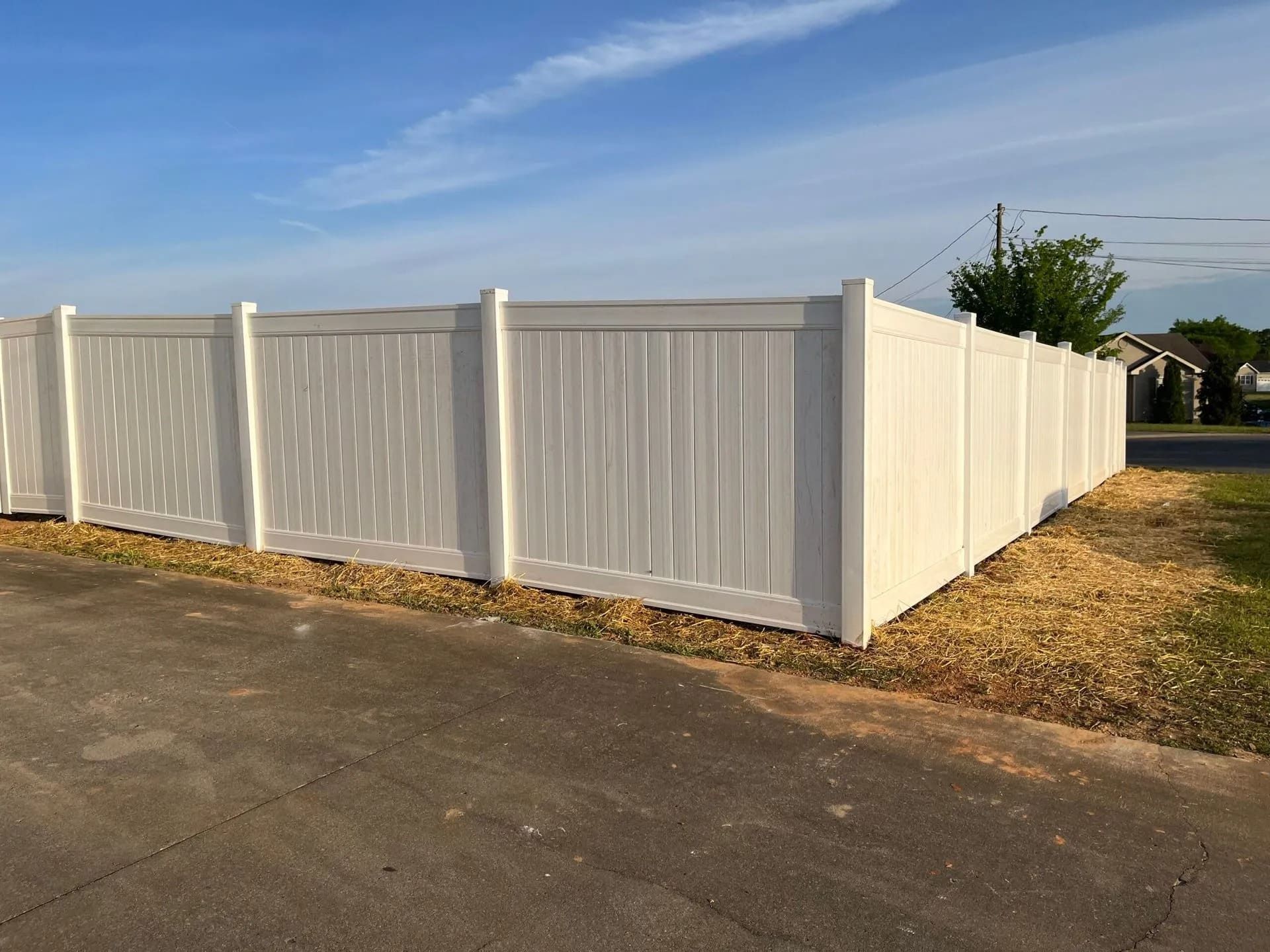 White vinyl fence in front of a blue sky, bordering a paved road by Allen's Tree and Fence.