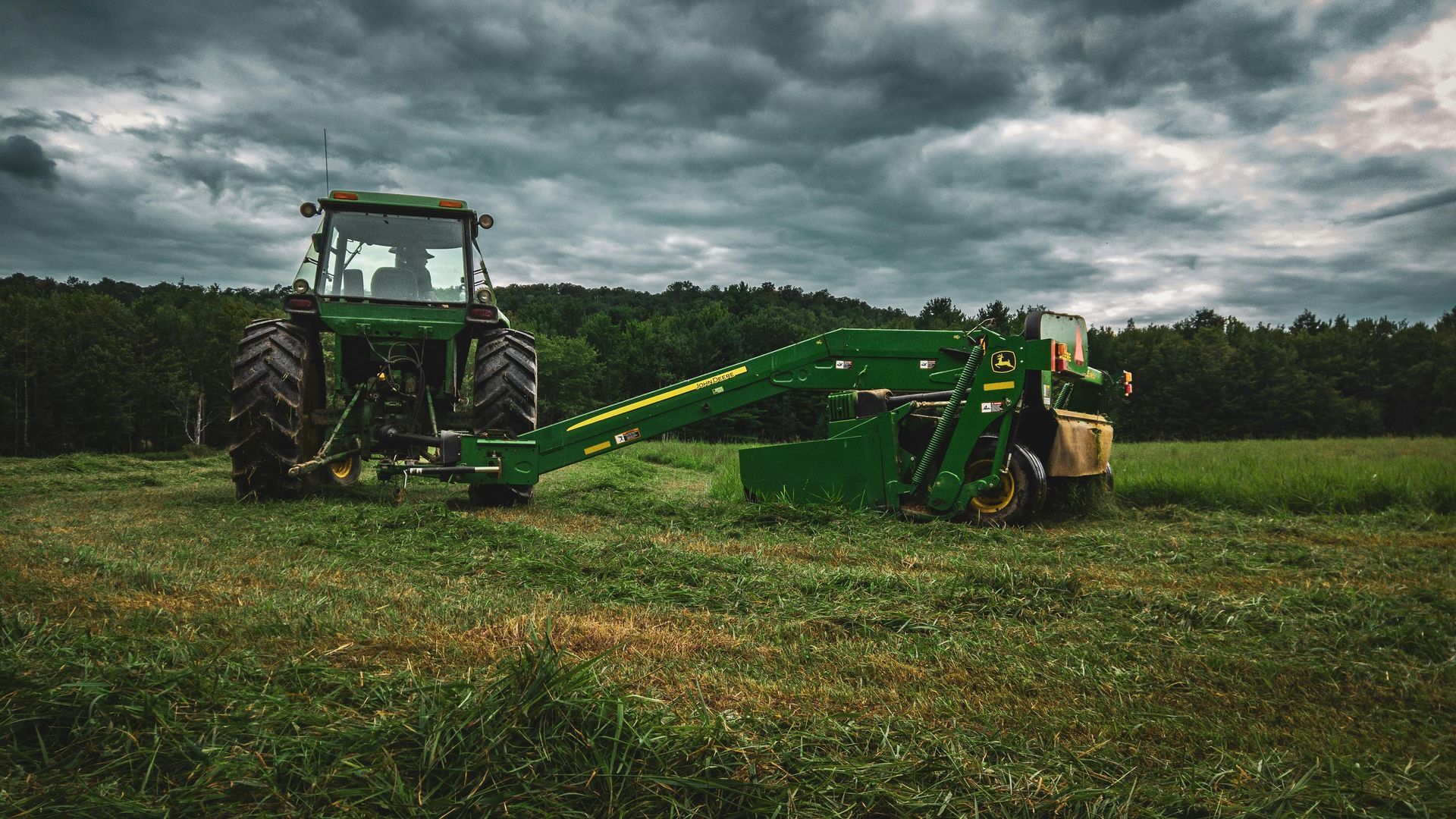 A John Deere tractor mowing a field of grass under a cloudy sky.