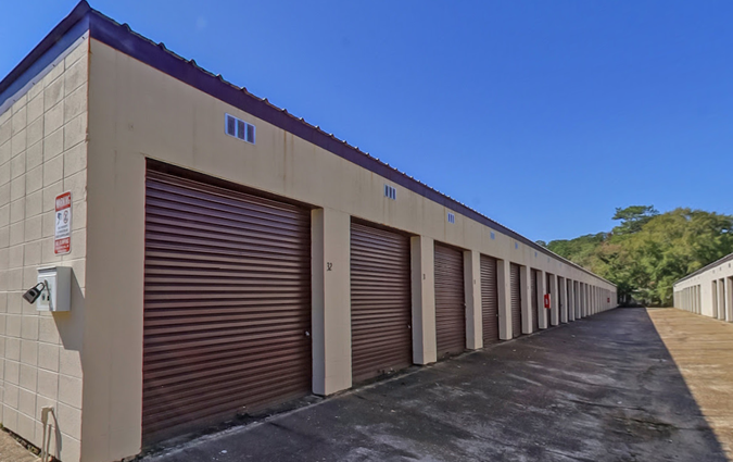 A row of beige storage units with brown roll-up doors against a clear blue sky.