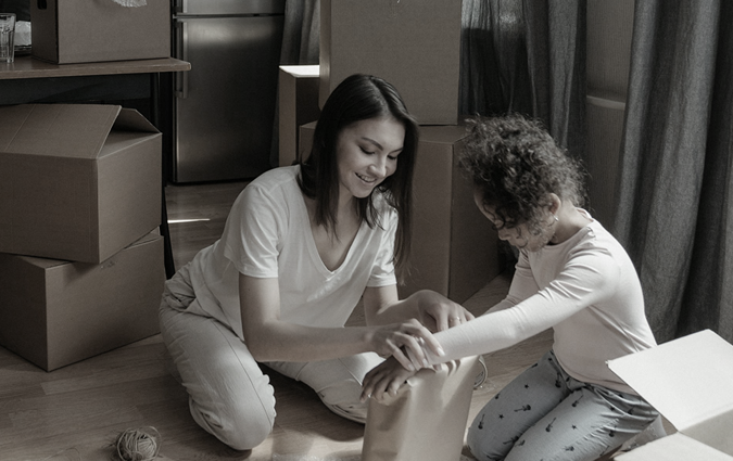 Woman and child kneeling, unpacking belongings from boxes.
