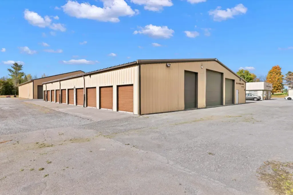 Beige storage building with multiple roll-up garage doors in a gravel lot under a blue sky