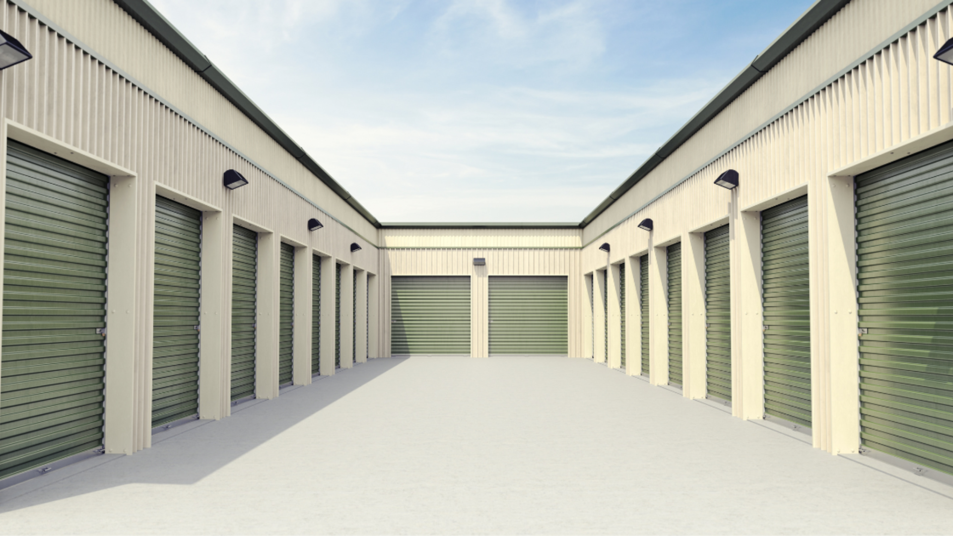 An outdoor self-storage facility with two rows of cream-colored units featuring green roll-up doors under a blue sky.