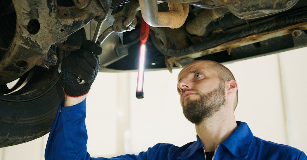 A man is working under a car with a flashlight. | JCruz Motors