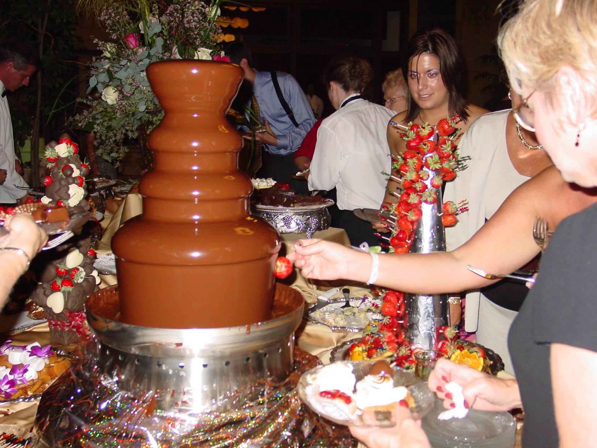 A woman is dipping a strawberry into a chocolate fountain