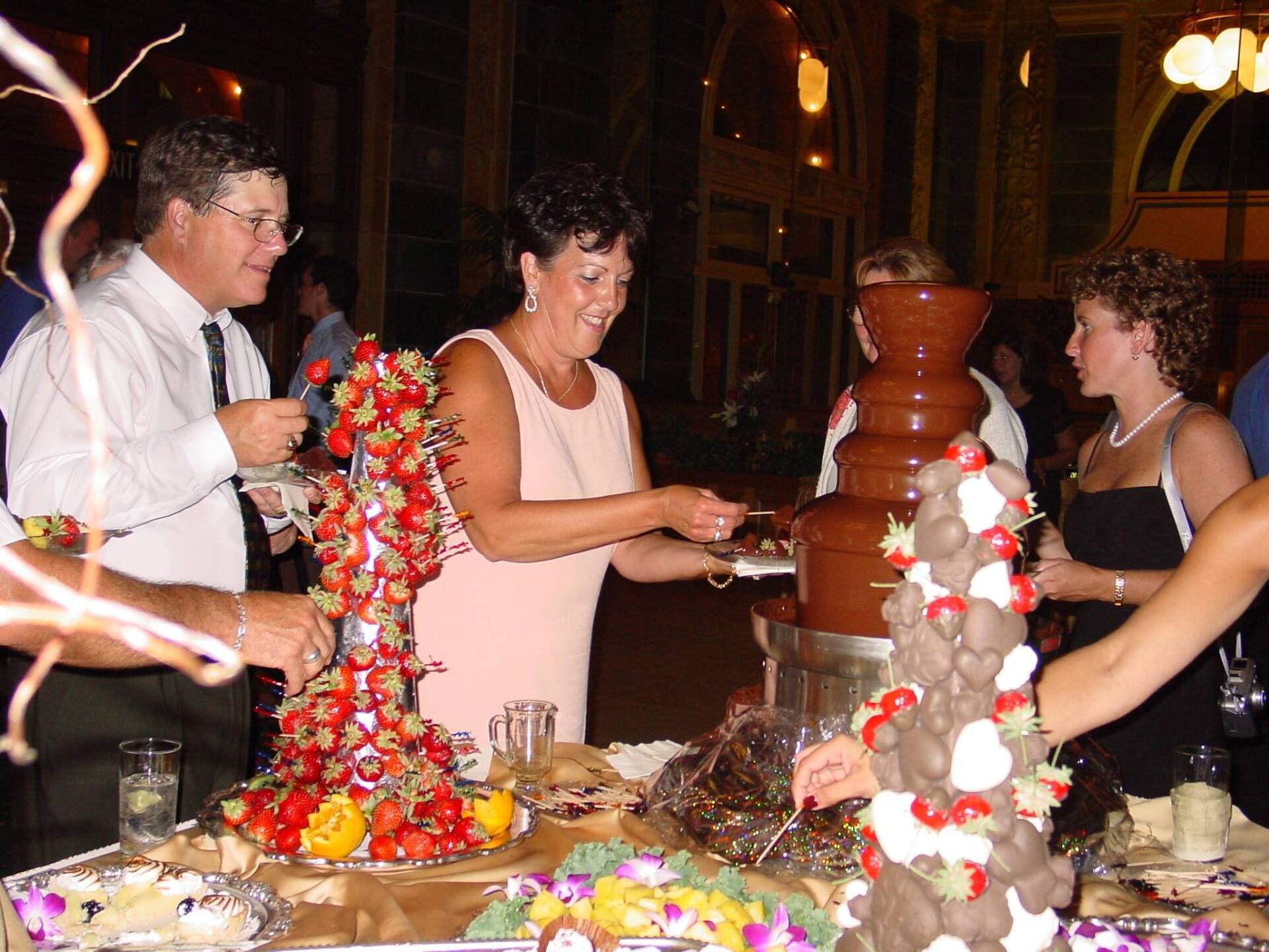 A group of people standing around a table with a chocolate fountain in the background