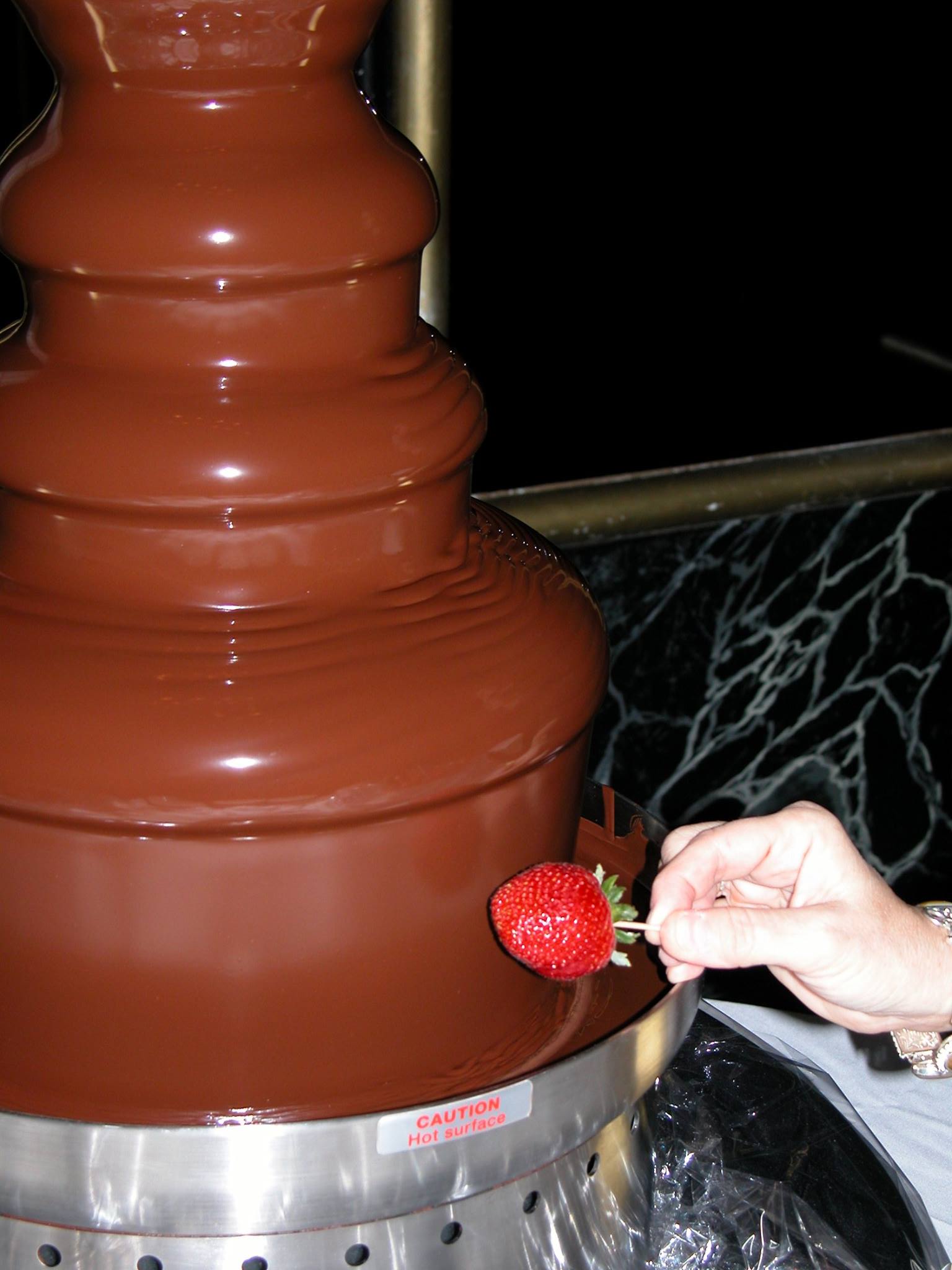 A person is dipping a strawberry into a chocolate fountain
