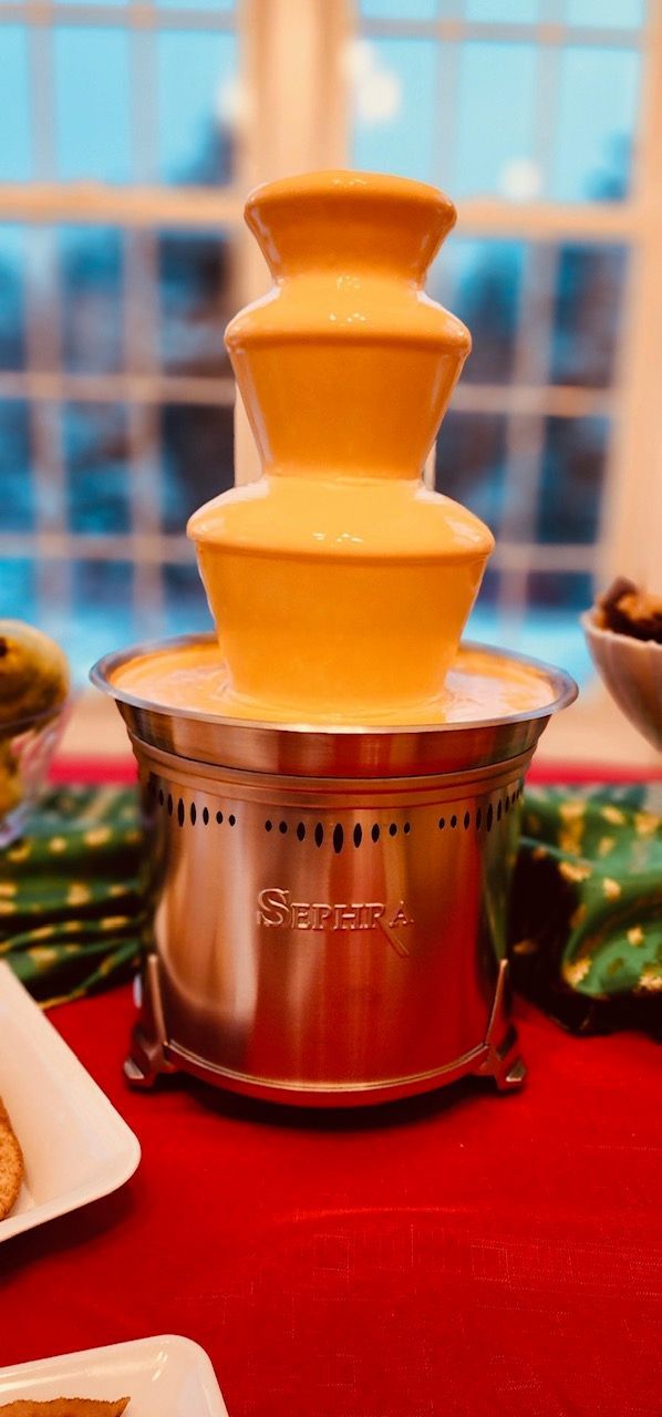 A chocolate fountain is sitting on a table next to a window.