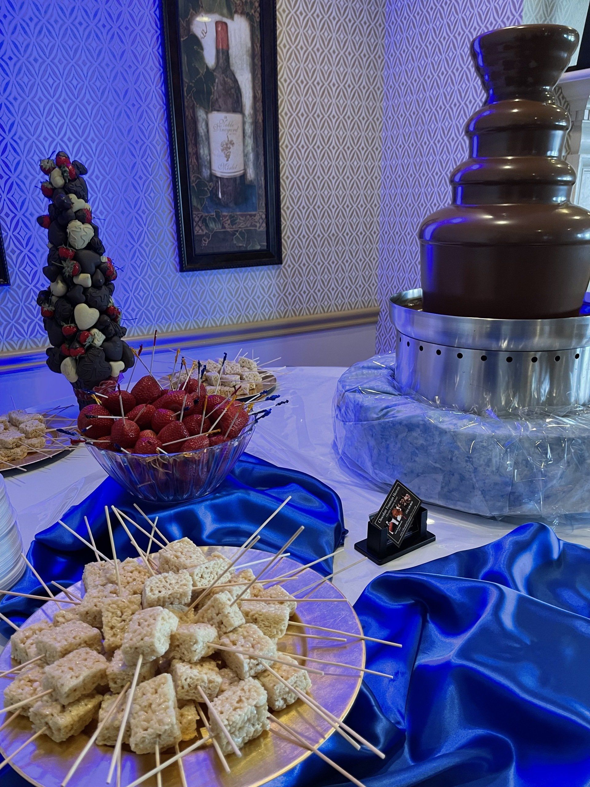 A table with a chocolate fountain and a bowl of strawberries on skewers.