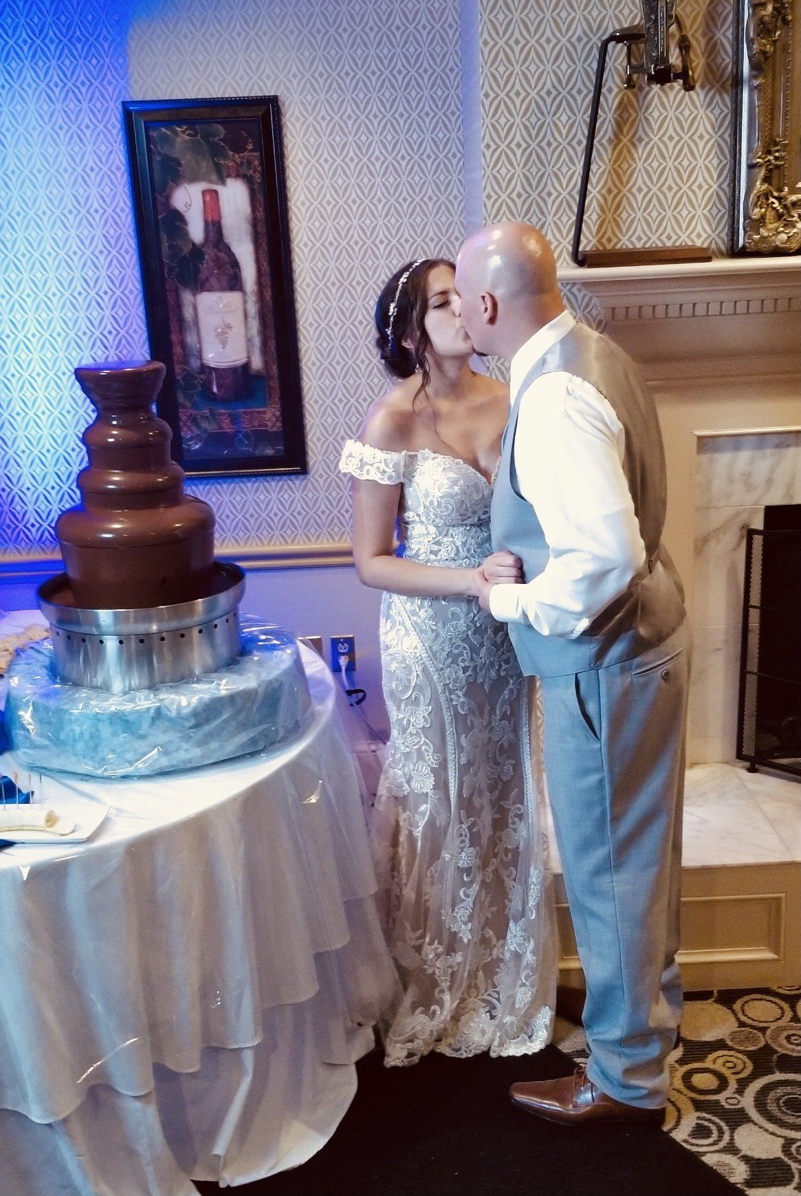 A bride and groom kissing in front of a chocolate fountain.