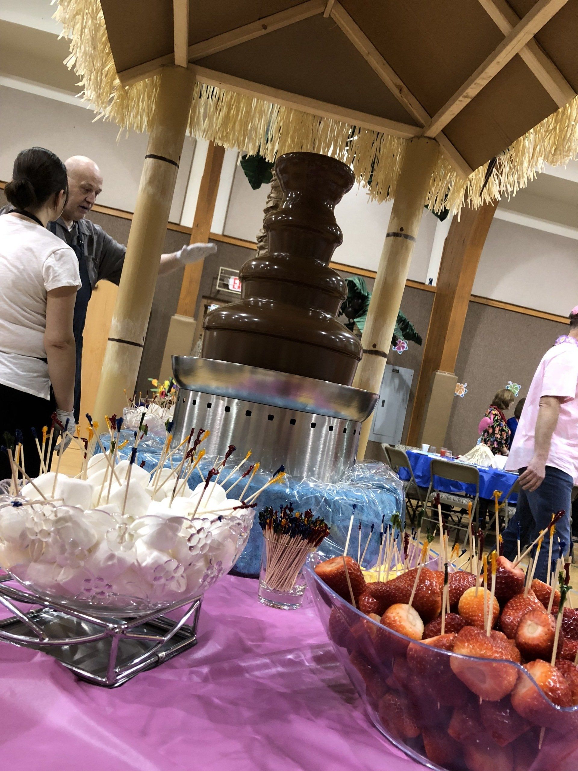 A group of people are standing around a table with a chocolate fountain in the background.