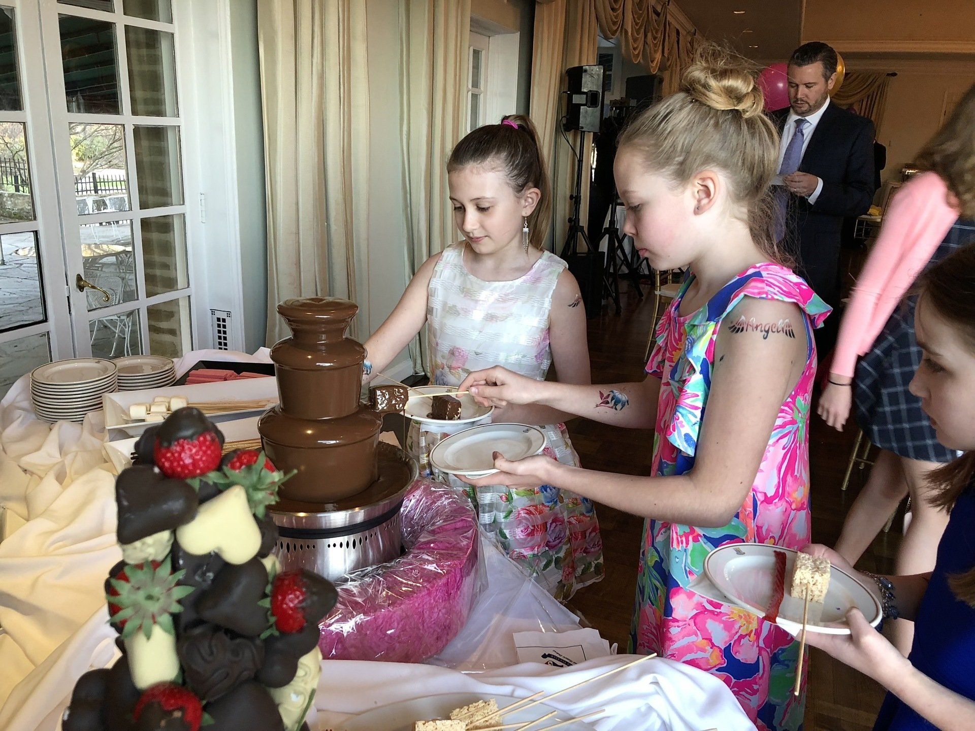Two young girls are standing in front of a chocolate fountain.