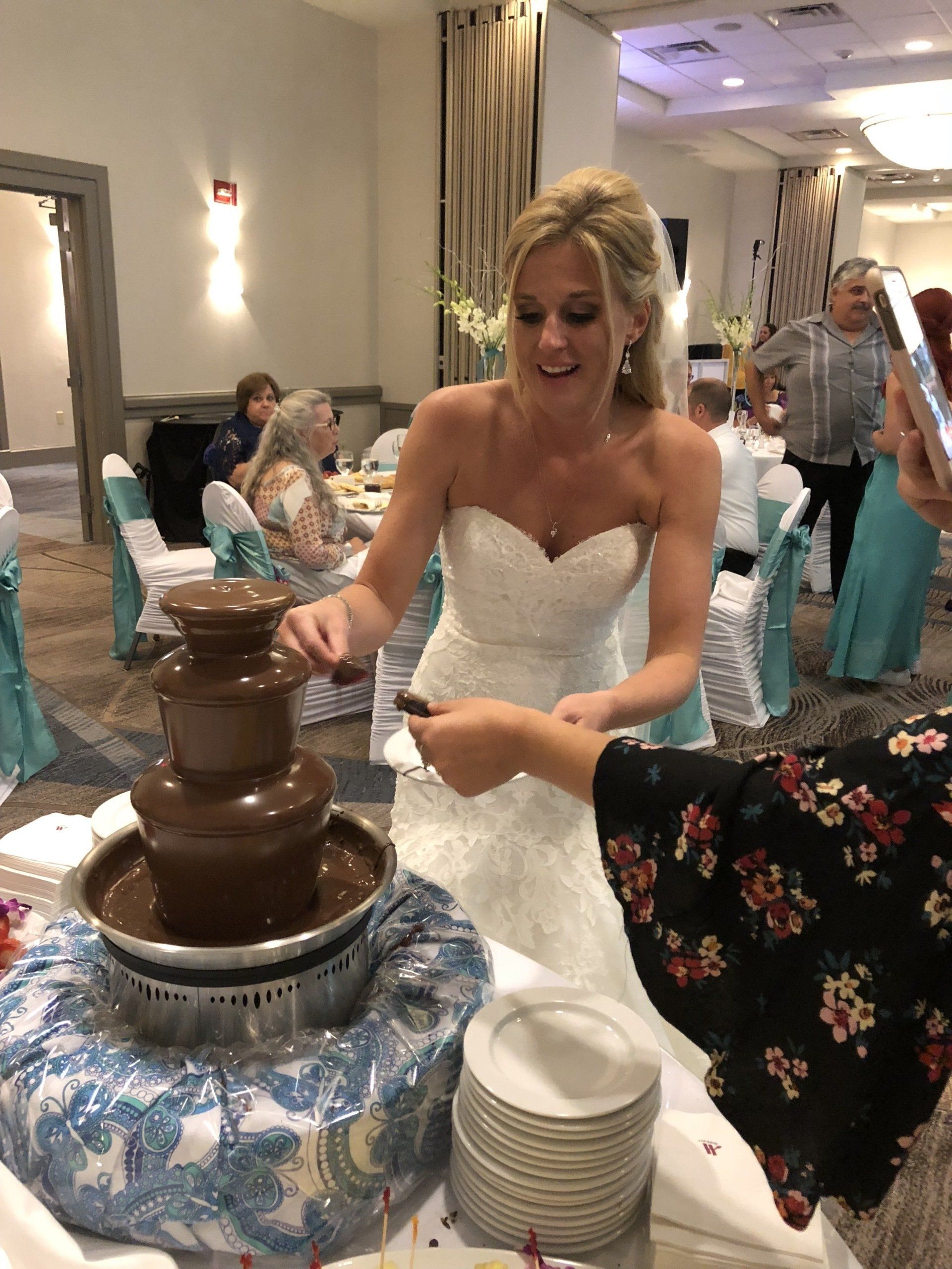 A woman in a wedding dress is cutting a chocolate fountain cake.