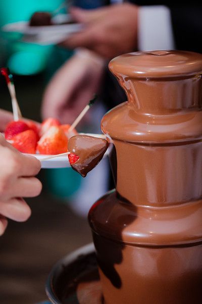 A person is dipping strawberries into a chocolate fountain.