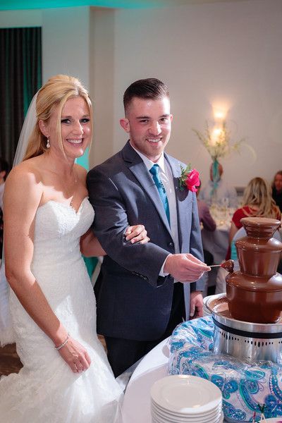 A bride and groom are cutting their wedding cake in front of a chocolate fountain.
