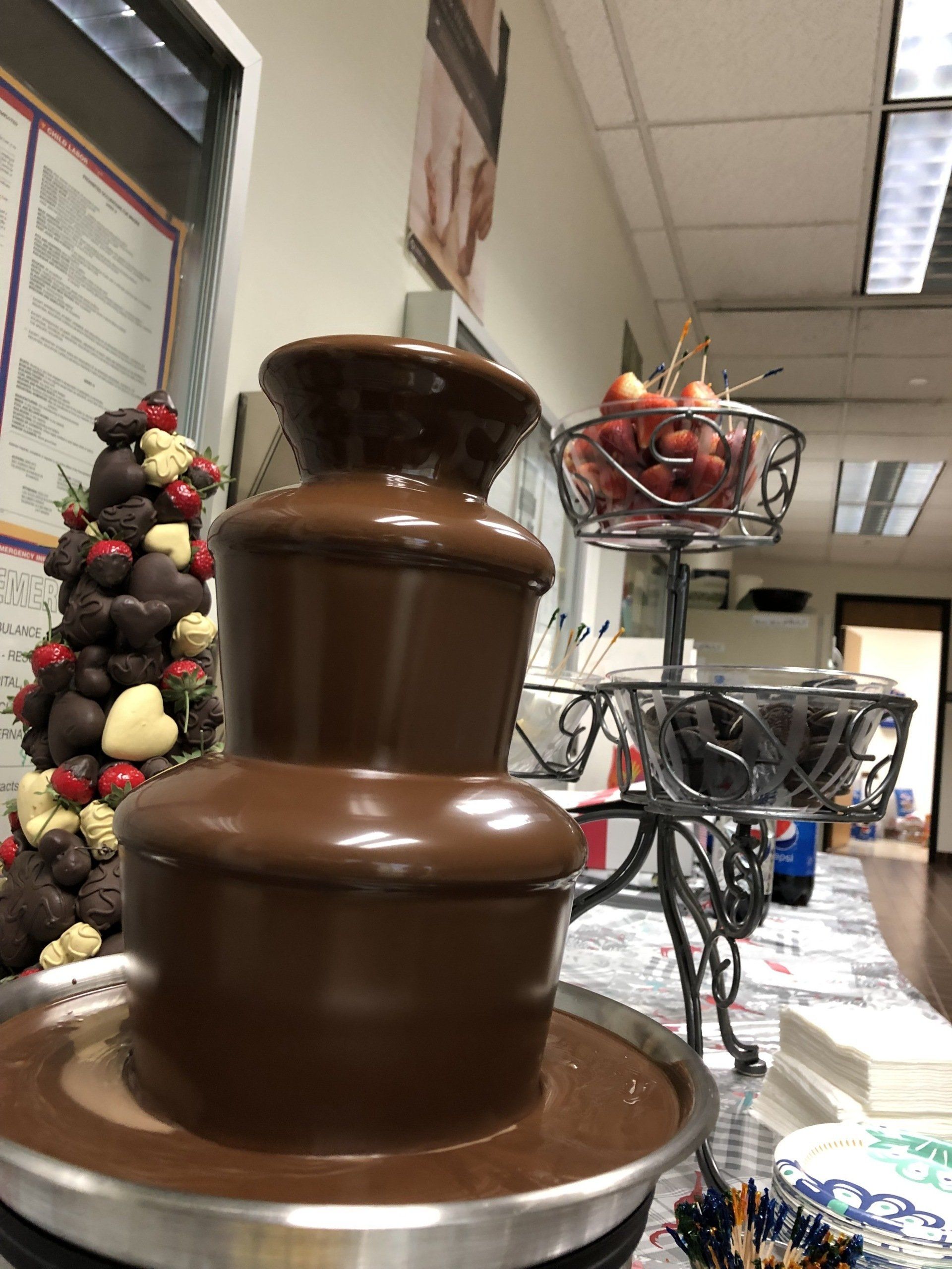 A chocolate fountain with strawberries on top of it is on a table.