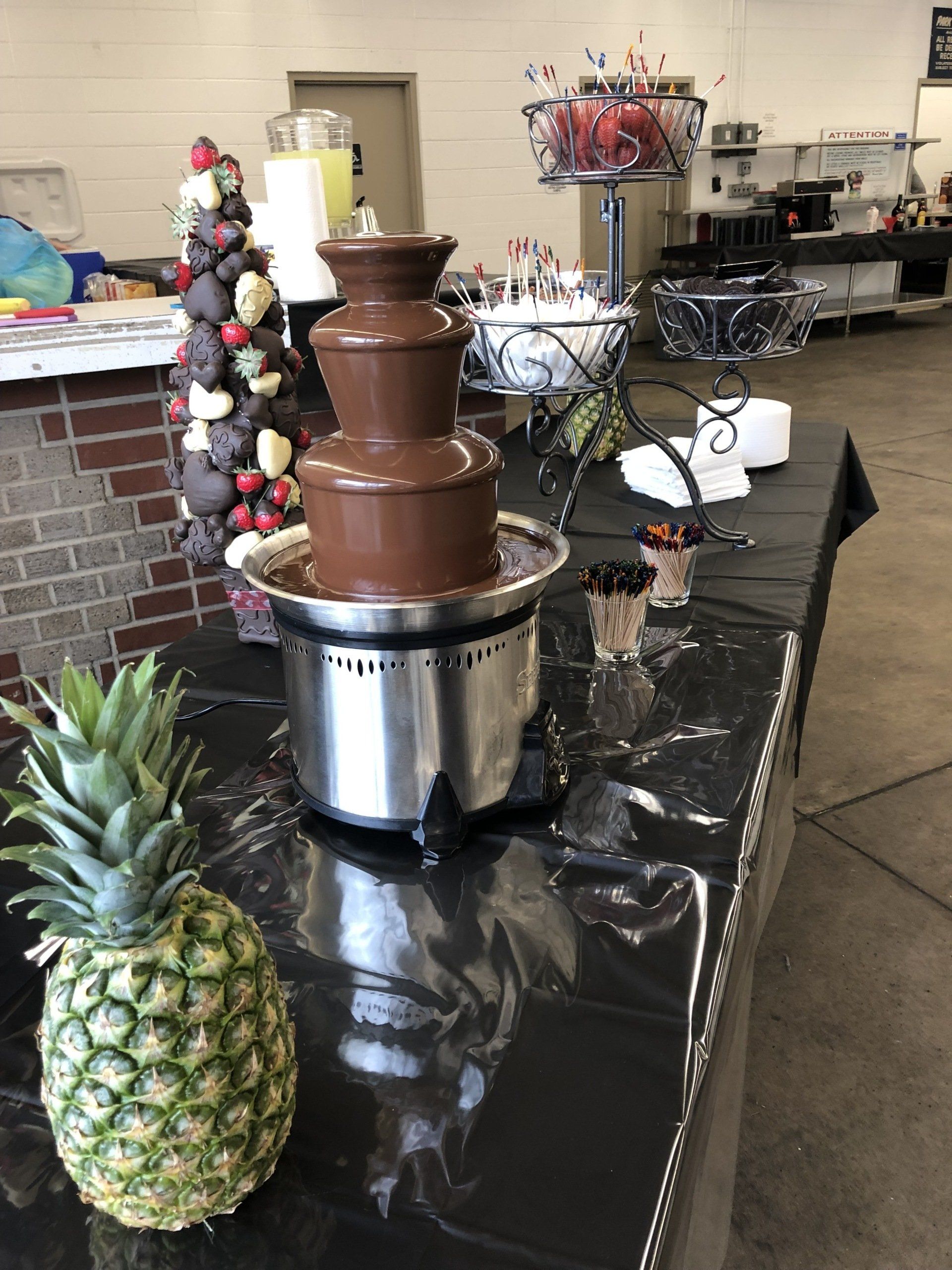 A chocolate fountain is sitting on a table next to a pineapple.