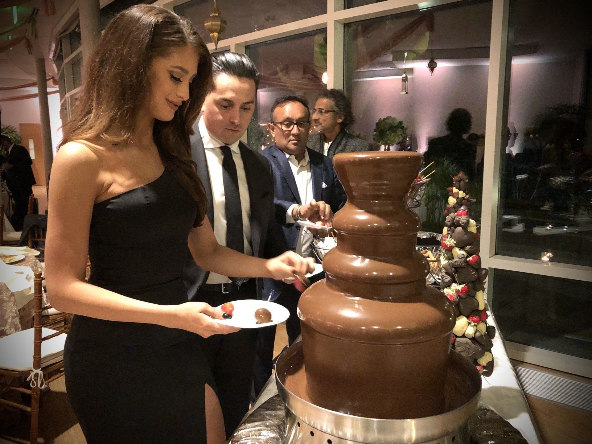 A woman in a black dress is standing next to a chocolate fountain.