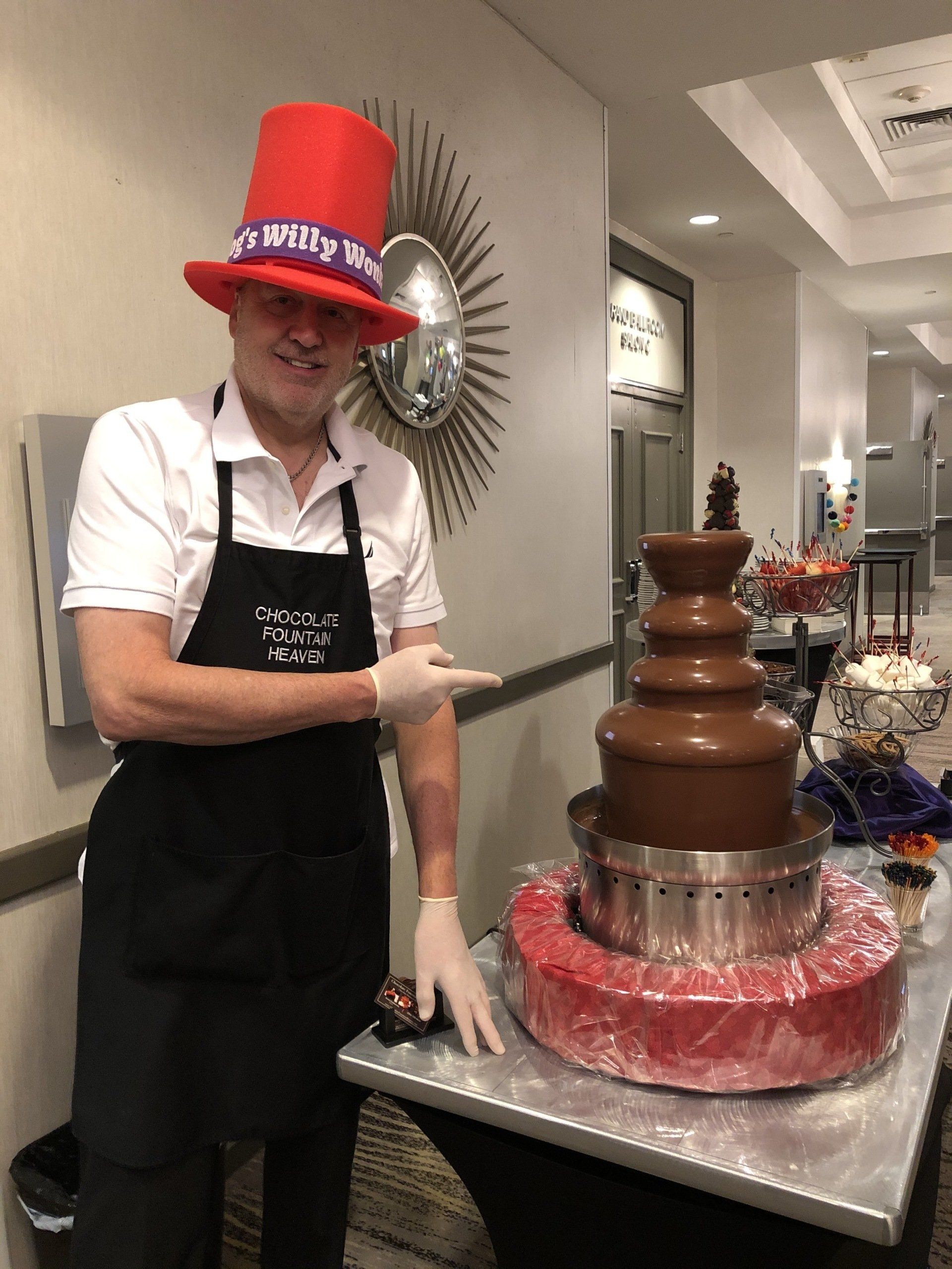 A man wearing a red top hat is standing next to a chocolate fountain.