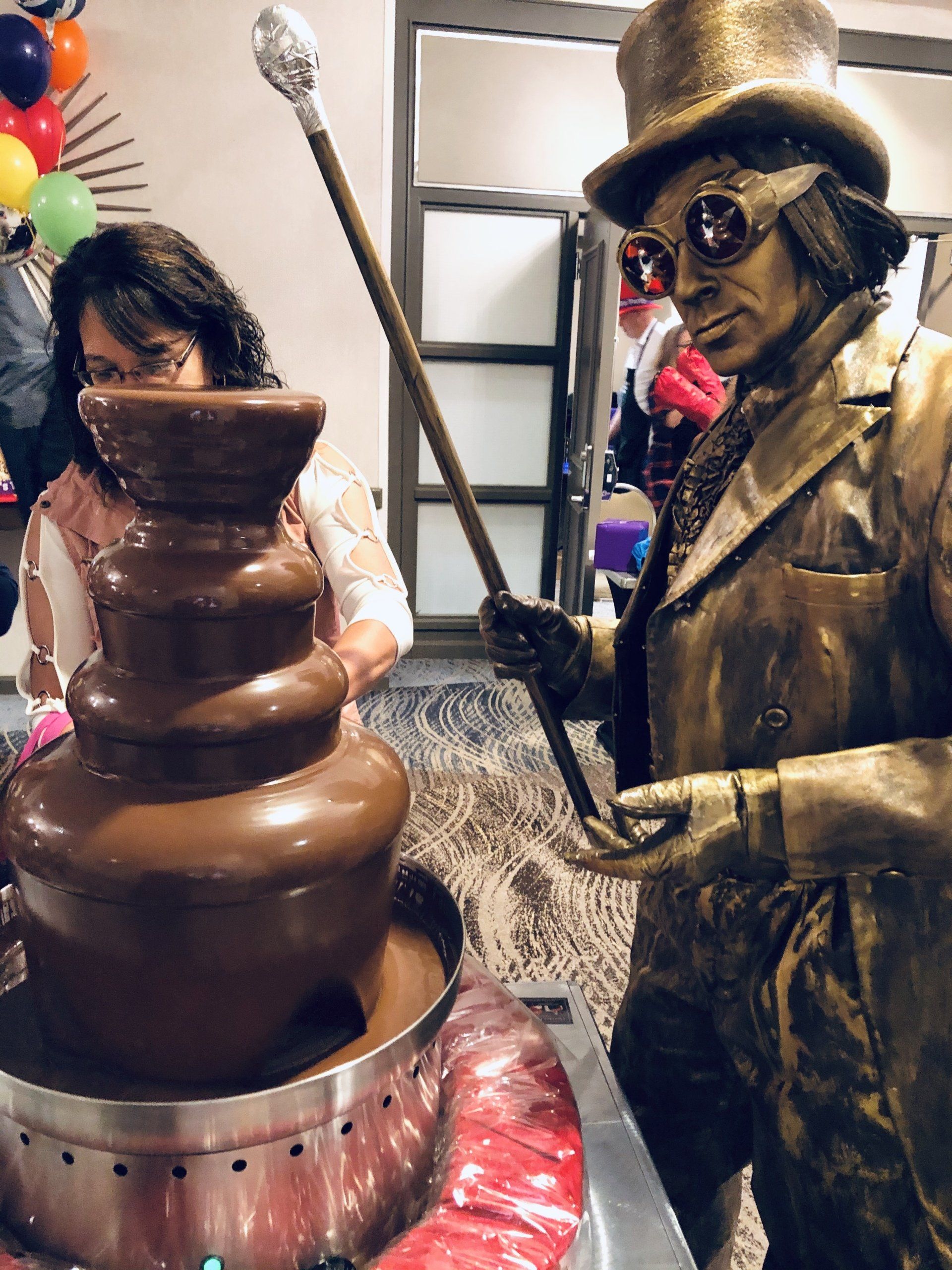 A statue of a man in a top hat is standing next to a chocolate fountain.