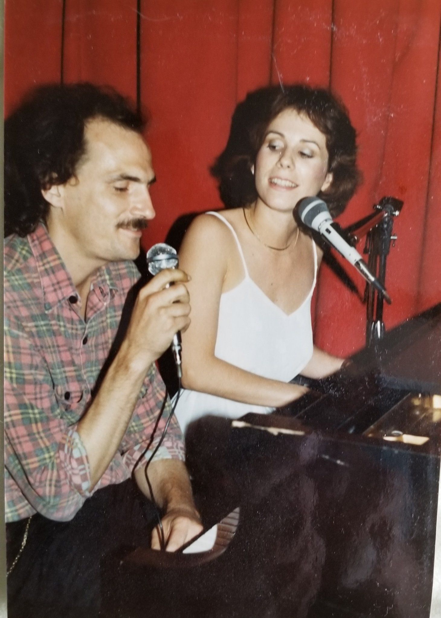 A man singing into a microphone next to a woman playing a piano