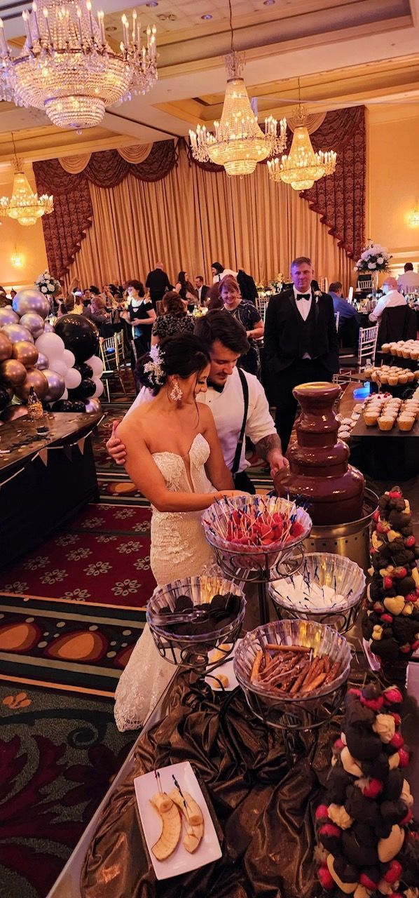 A bride and groom are cutting their wedding cake in front of a chocolate fountain.