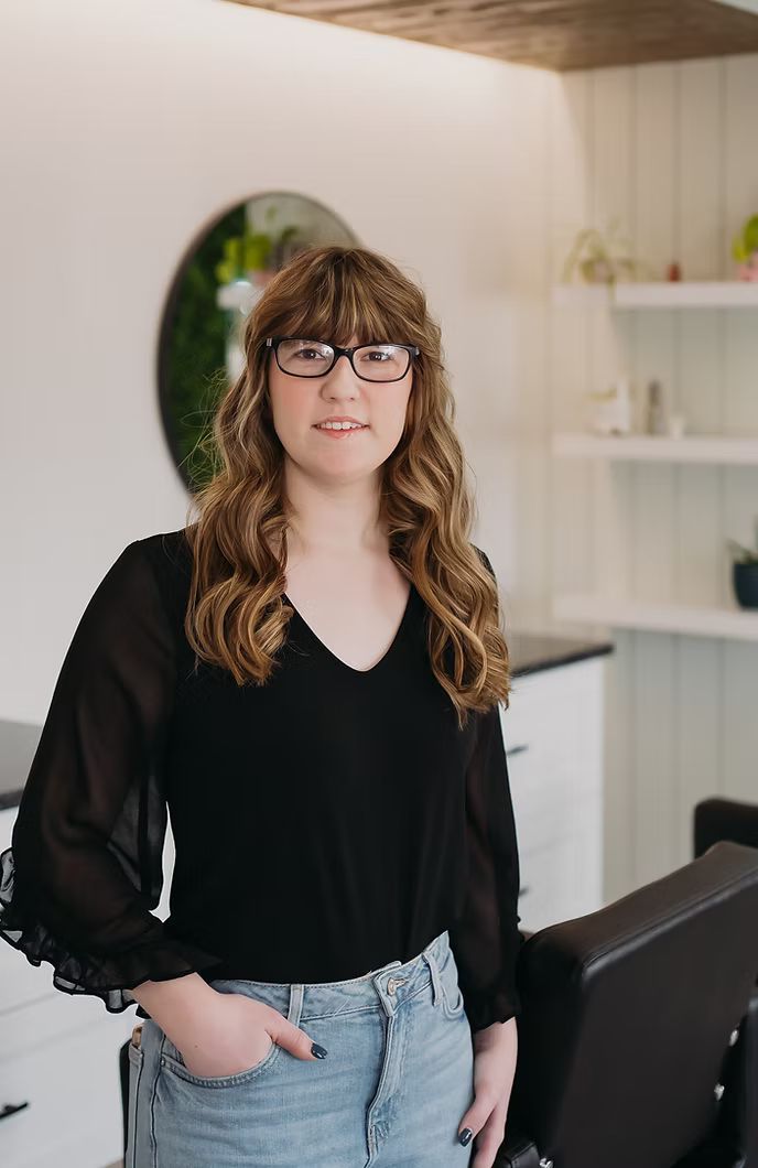 A woman wearing glasses and a black shirt is standing in a salon.