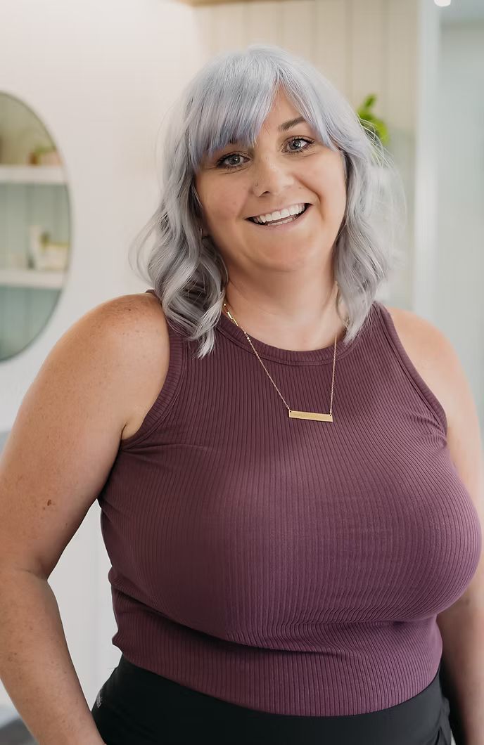 A woman with gray hair is wearing a purple tank top and a necklace.