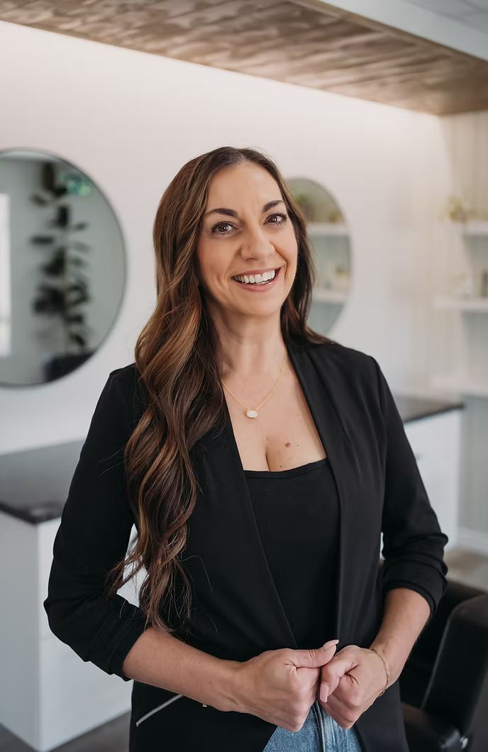 A woman in a black jacket is standing in a room and smiling.